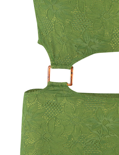 Close-up of the TIGERMIST AANYA DRESS - GREEN, showcasing its elegant green lace fabric with a floral pattern and a small gold rectangular metal connector joining two pieces of the material. The intricate lace details beautifully highlight the texture and design of this sophisticated green jersey dress with an exquisite lace overlay.