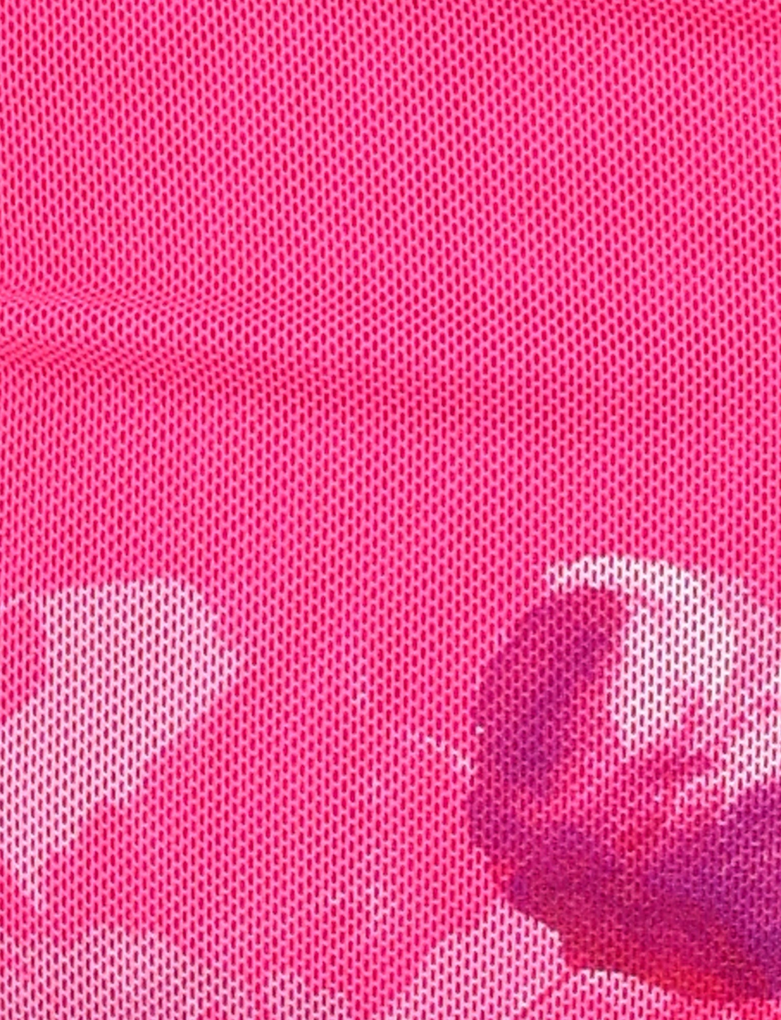 The ACADIA TOP - PINK : HOT PINK from TIGERMIST features a delicate mesh fabric with a pattern of small, evenly spaced holes. Beyond the mesh, indistinct objects are visible, including a partially obscured round, shiny item reflecting light on the bottom right side of the image. The material showcases intricate mesh fabrication techniques.